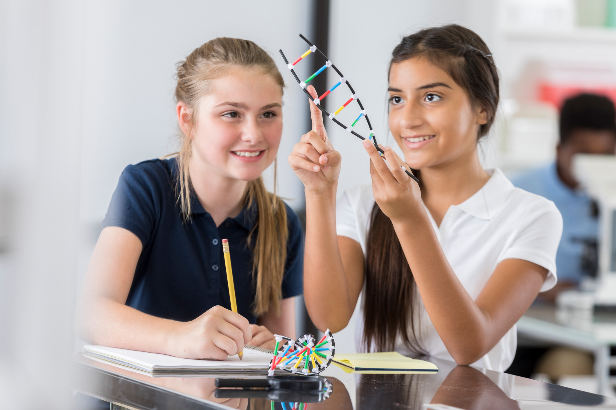 high school girls examine a DNA helix model. One of the students is pointing to something on the helix.