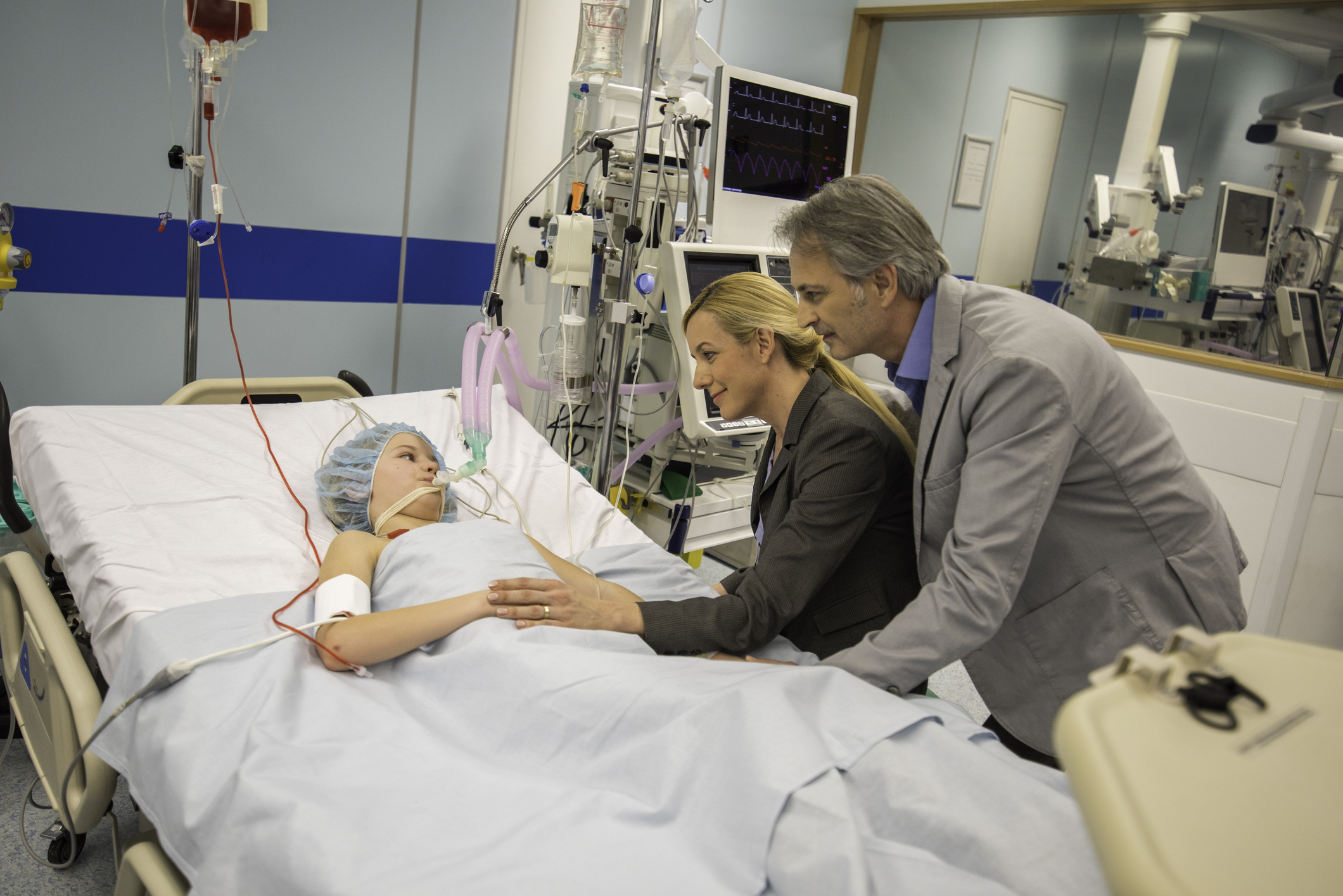 Young boy in ER lying on bed with worried parents beside the bed.